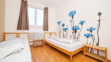 Un dormitorio con dos camas, un radiador, una ventana con cortinas y una pared decorada con motivos florales.
