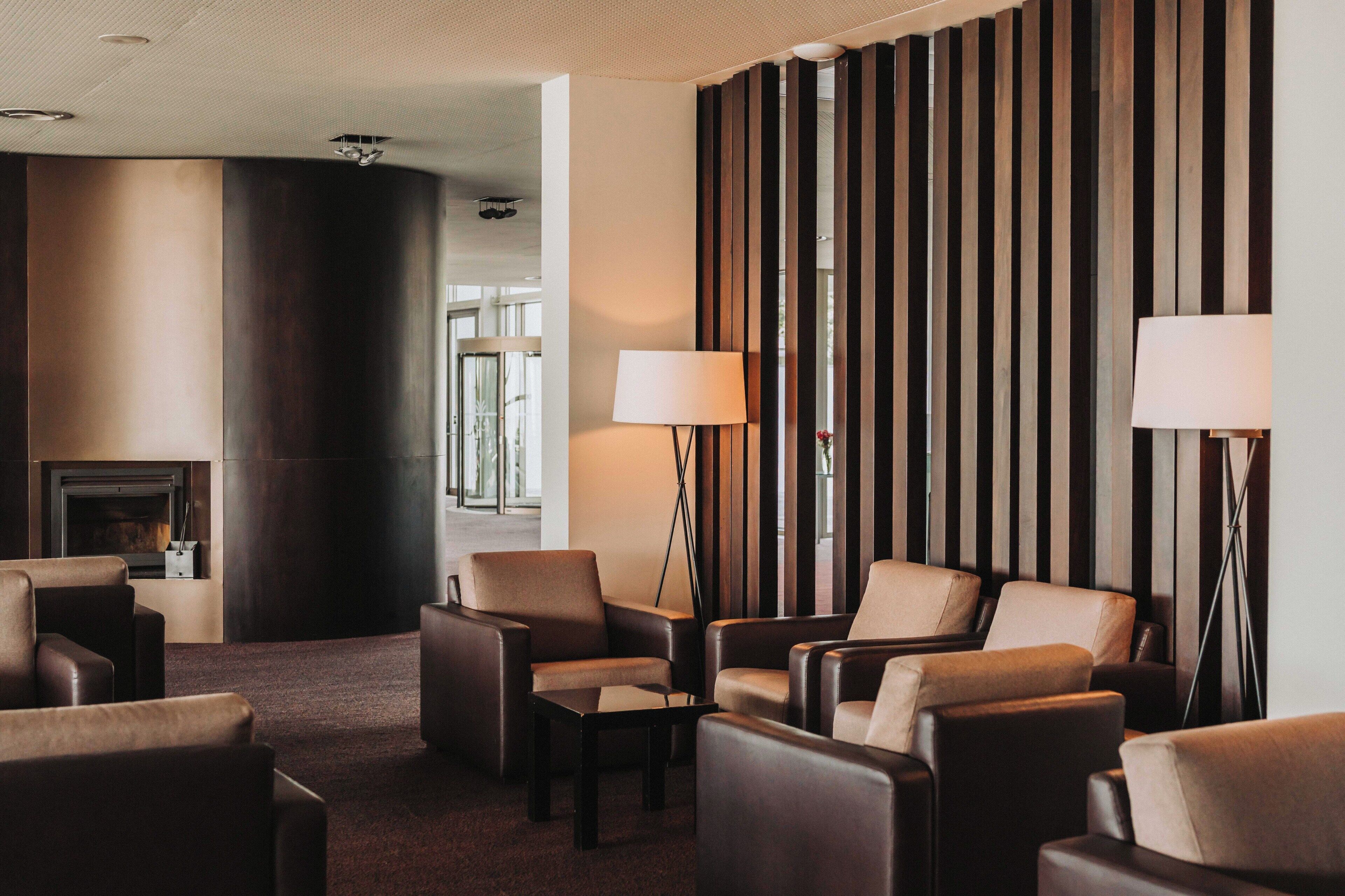 A modern hotel lobby with leather sofas, a fireplace, and tall wooden panels.