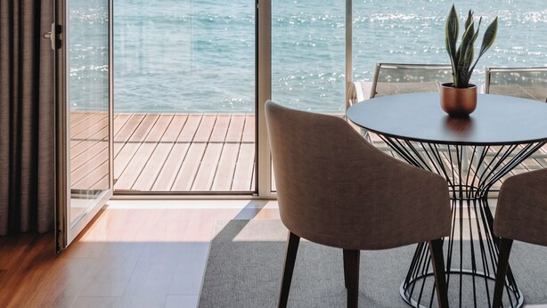 Een balkon met uitzicht op zee, een tafel met stoelen en een bloempot.