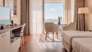 Een hotelkamer met een bed, bureau, stoel, televisie, lamp en uitzicht op de oceaan.