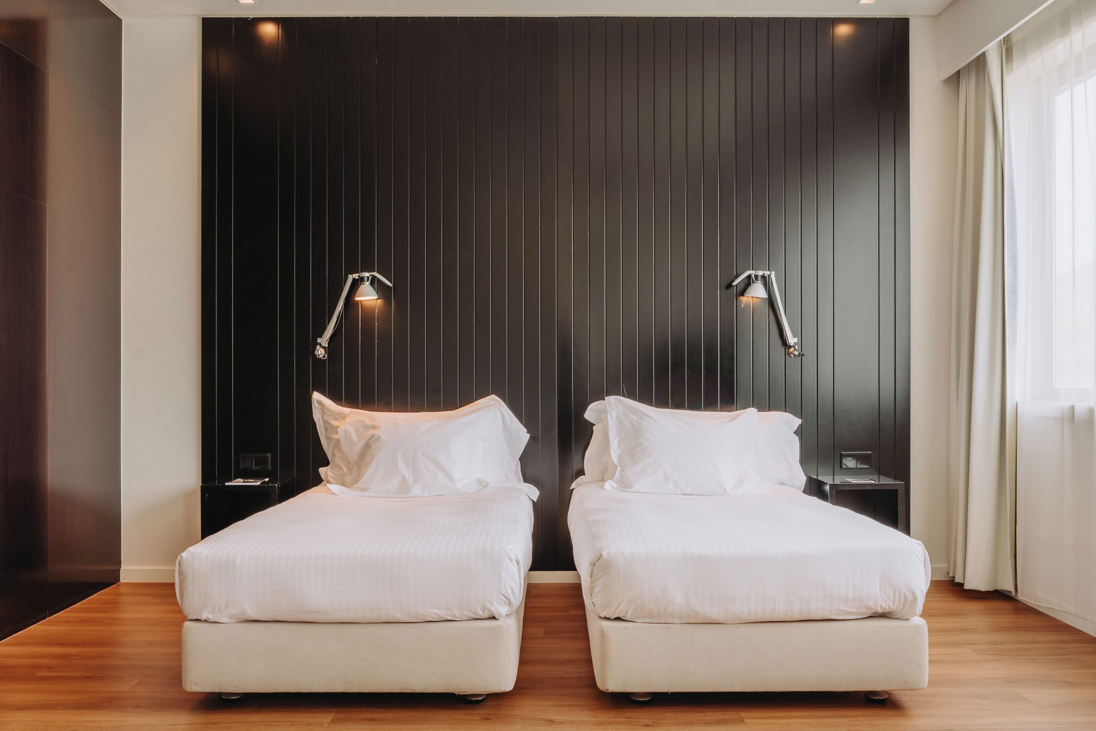 Una habitación de hotel moderna con dos camas individuales, paneles de madera oscura en las paredes y lámparas de noche.