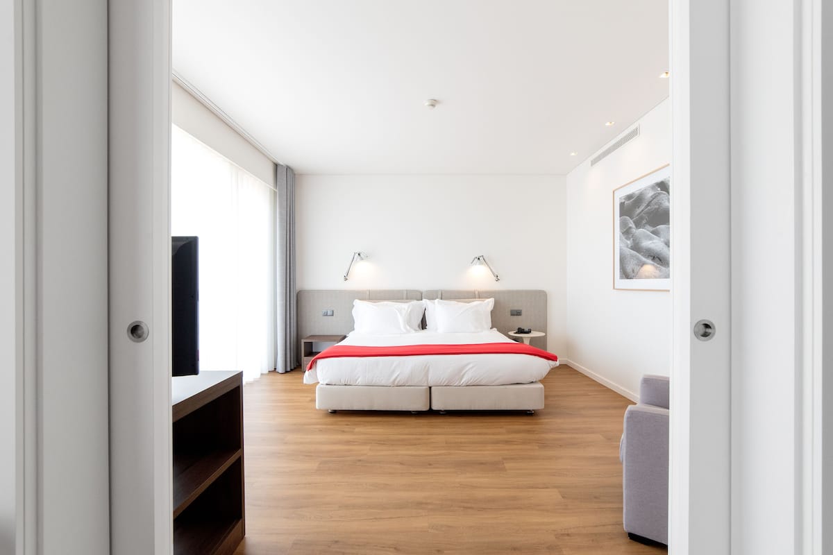 Een moderne hotelkamer met een groot bed, bedlampen, een flatscreen televisie en een ingelijste foto aan de muur.