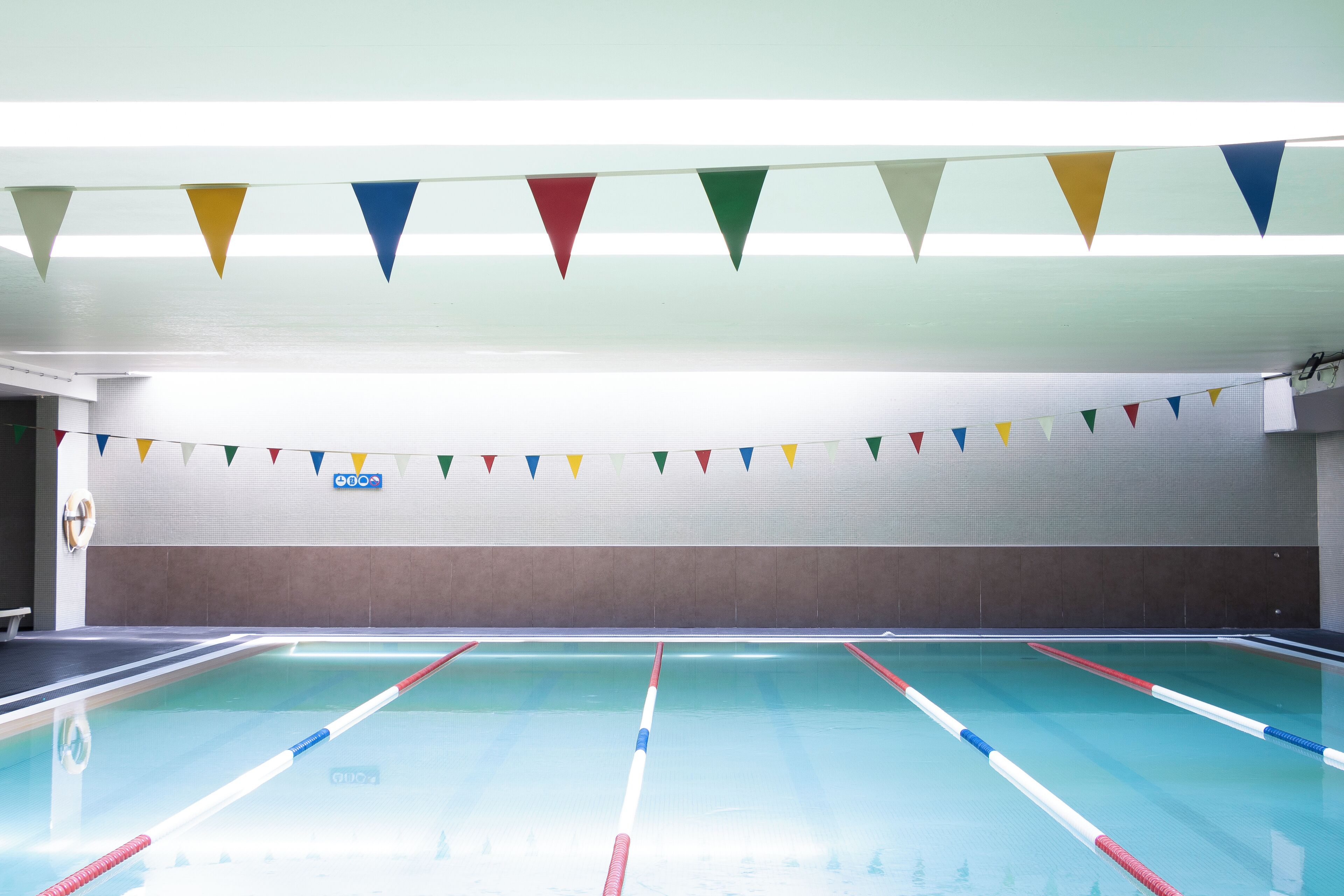 Una piscina interior con separadores de carril y coloridas banderas triangulares en el techo.