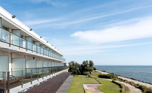 A modern building with a glass facade, a long bench area, and a view of the sea.