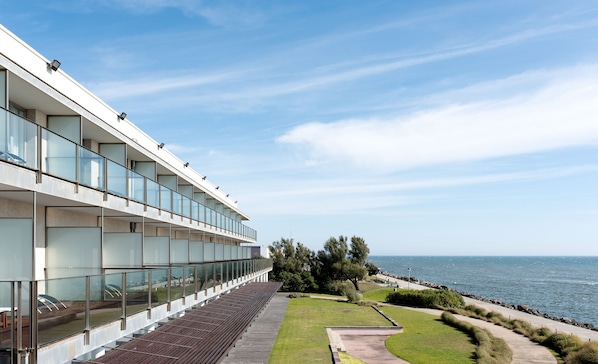 A modern building with a glass facade, a long bench area, and a view of the sea. - Hotel Flôr de Sal by The Editory (Viana do Castelo)