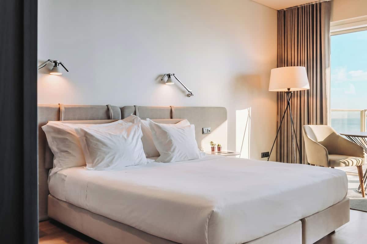 Een hotelkamer met een bed, bedlampjes, een stoel en uitzicht op de lucht.