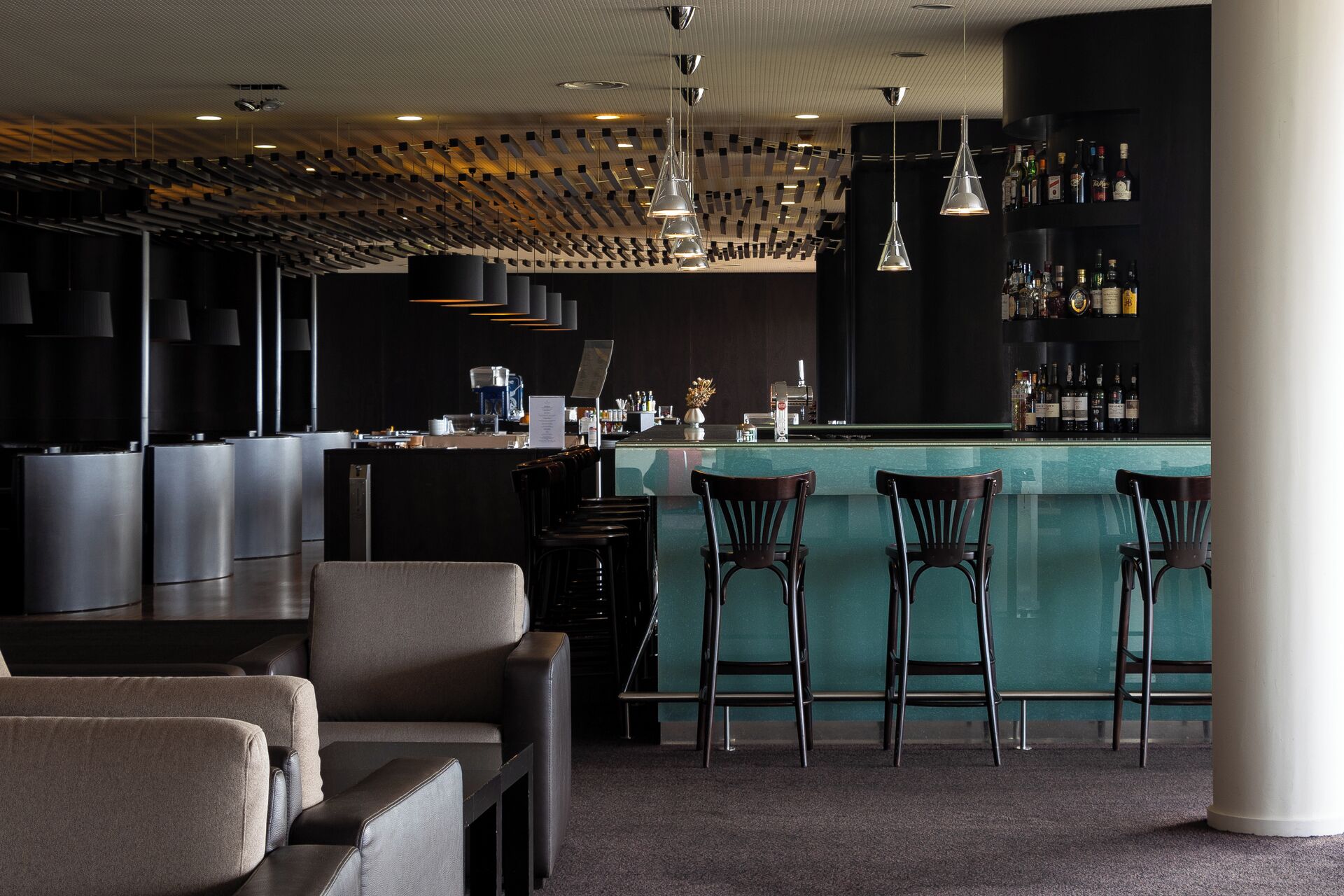 A modern bar area with a bar counter, multiple stools, and a seating area with sofas.