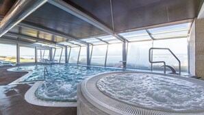 Een modern binnenzwembad met glazen wanden, een whirlpool en uitzicht op zee.