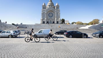 A large cathedral with a prominent circular window and two towers, surrounded by a paved area with cars and bicycles.