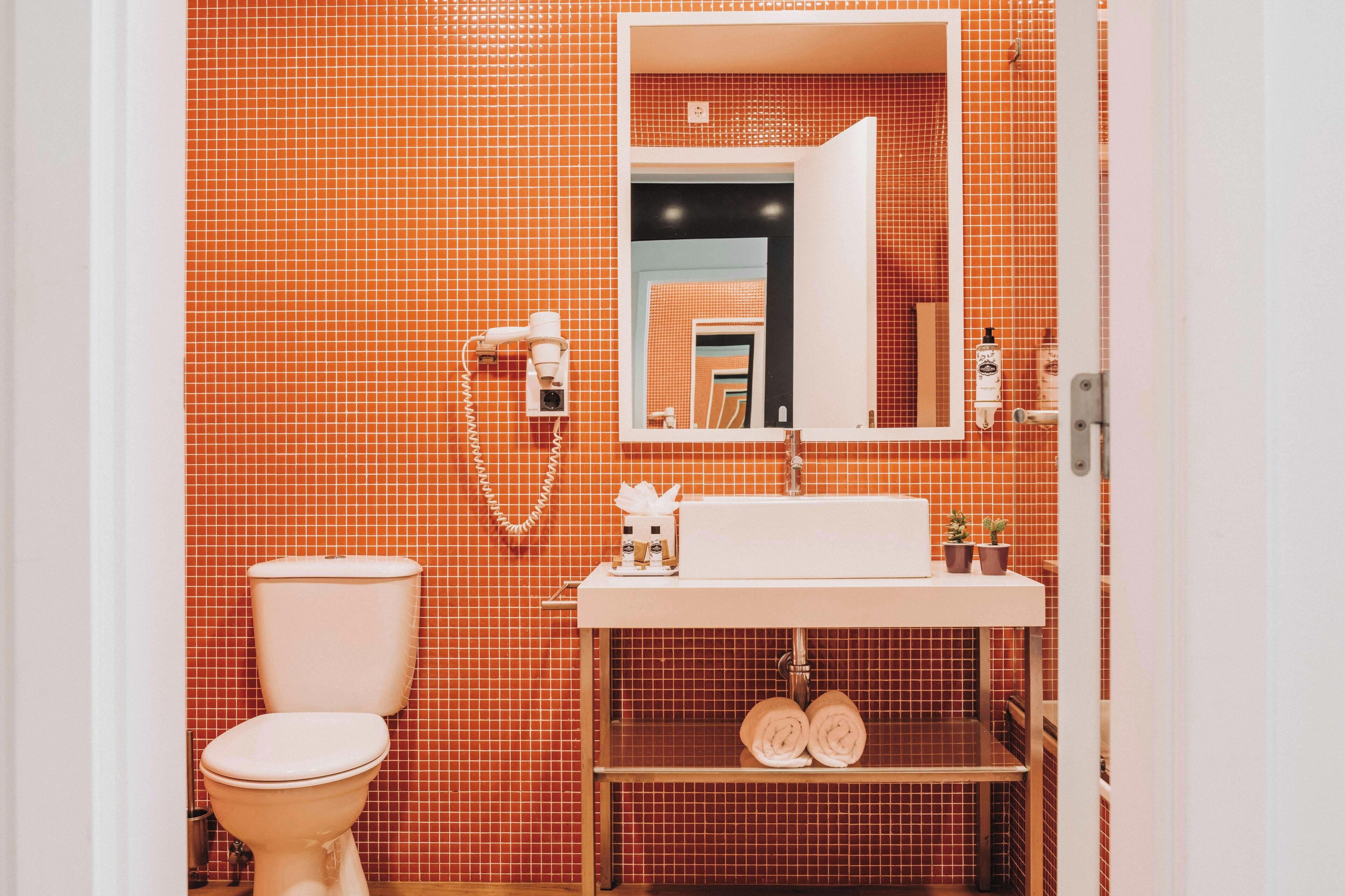 Une salle de bain équipée de toilettes, d’un lavabo, d’un miroir et de murs carrelés.