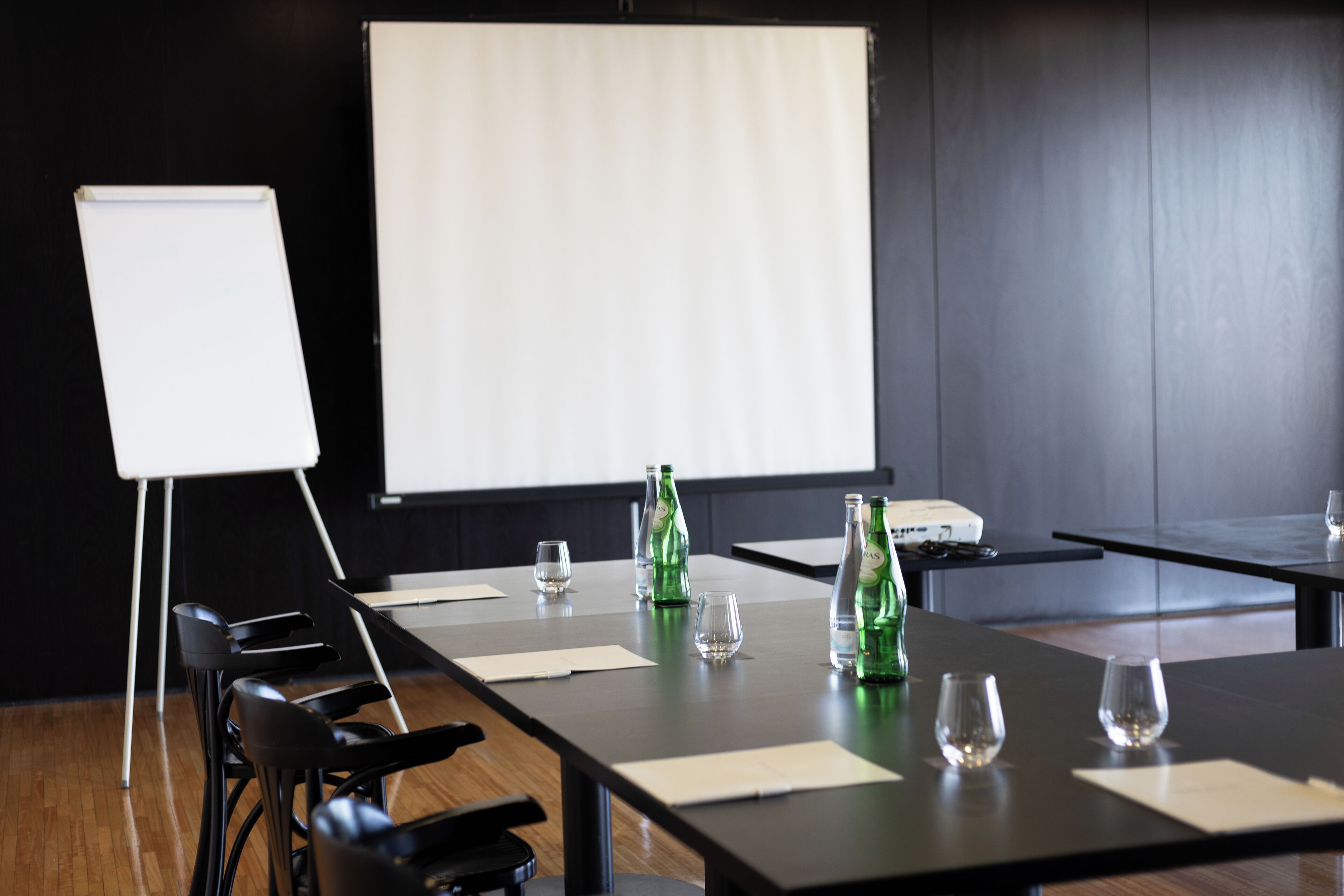 A conference room with a long table, chairs, a projector screen, and a whiteboard.