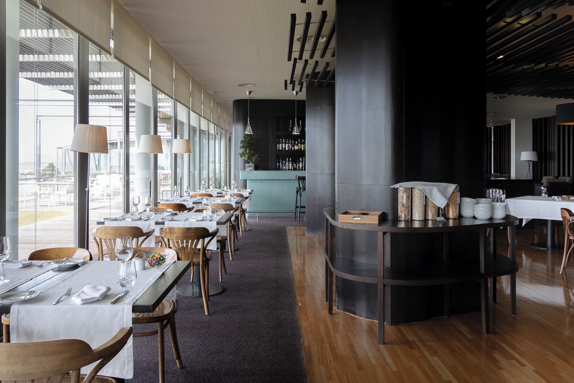 Un restaurant moderne avec de longues tables, des chaises en bois et un coin bar.