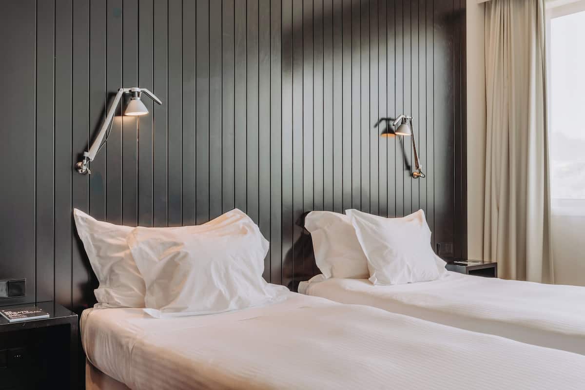 Een hotelkamer met twee bedden, donker houten paneelbekleding en twee wandlampen.
