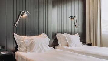 A hotel room with two beds, dark wooden paneling, and two wall-mounted reading lamps.