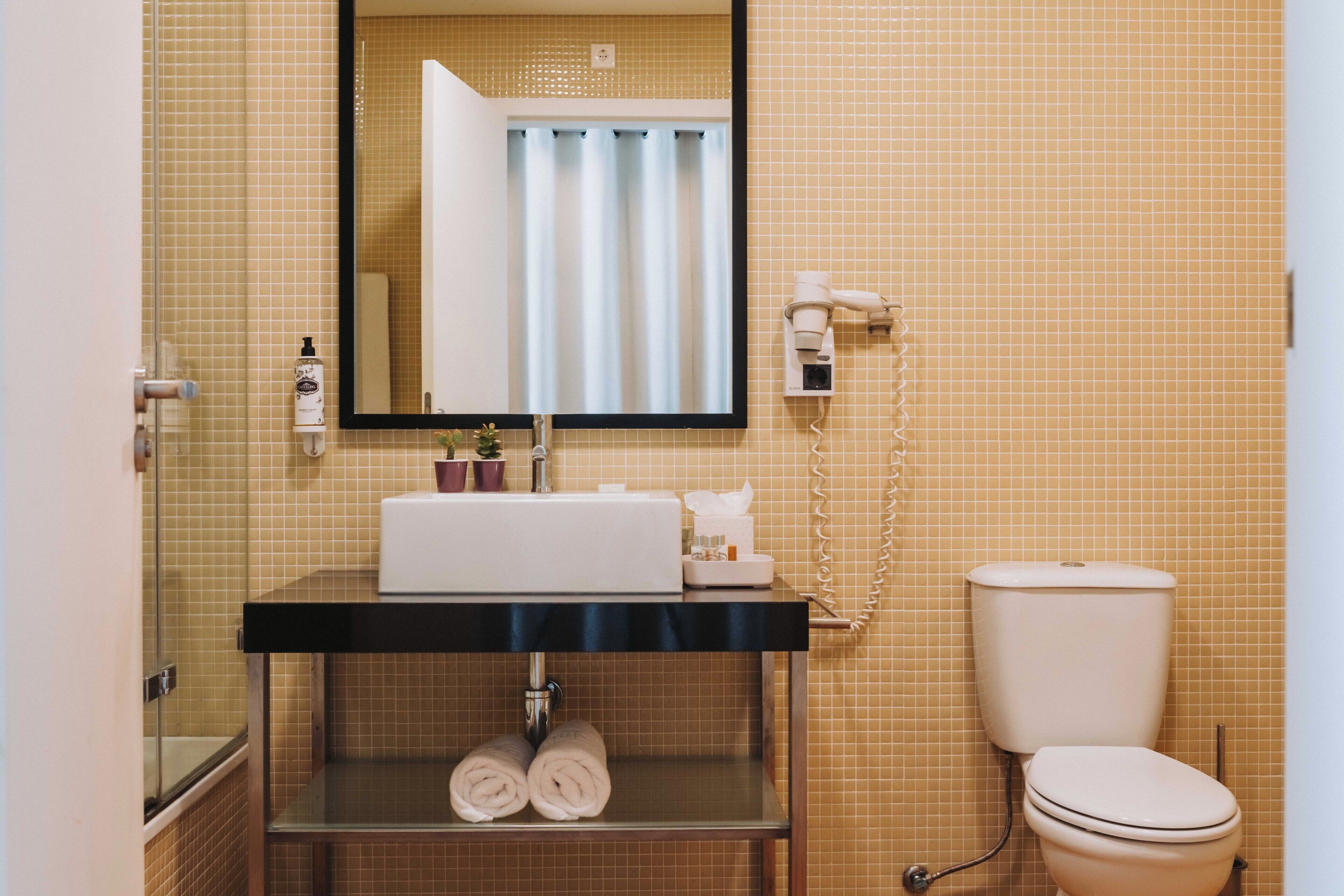 A bathroom with a sink, mirror, toilet, and a shower area.
