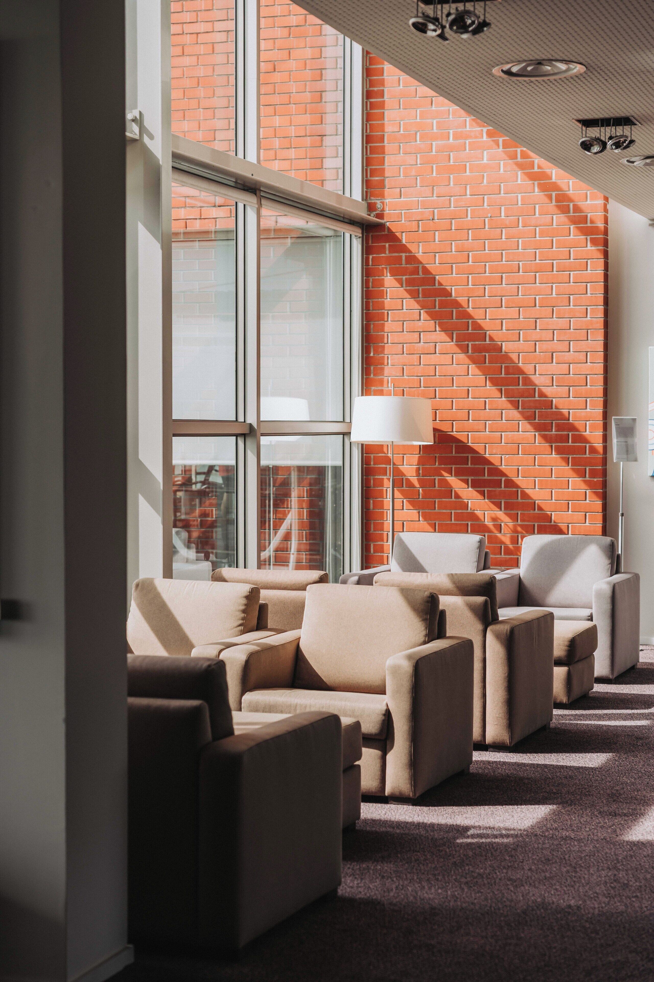 Ein modernes Interieur mit Backsteinwand, großen Fenstern und einer Sitzecke mit Sofas und einer Stehlampe.