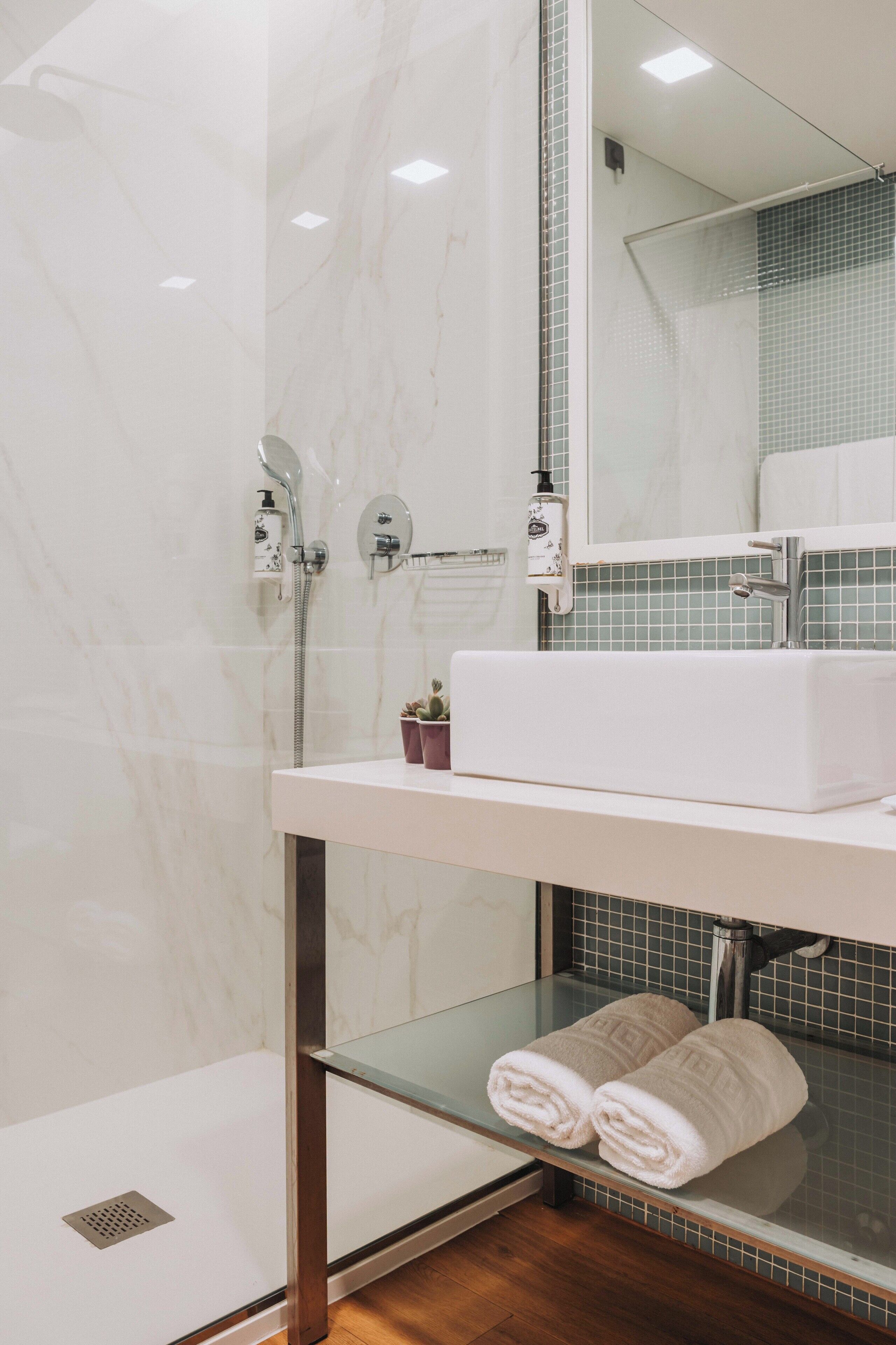 A bathroom with a shower, a sink, a mirror, and a glass shelf with towels.