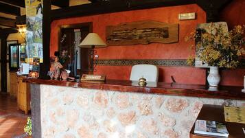 A reception area with a stone wall, wooden reception desk, a lamp, a framed picture, and a vase with flowers.