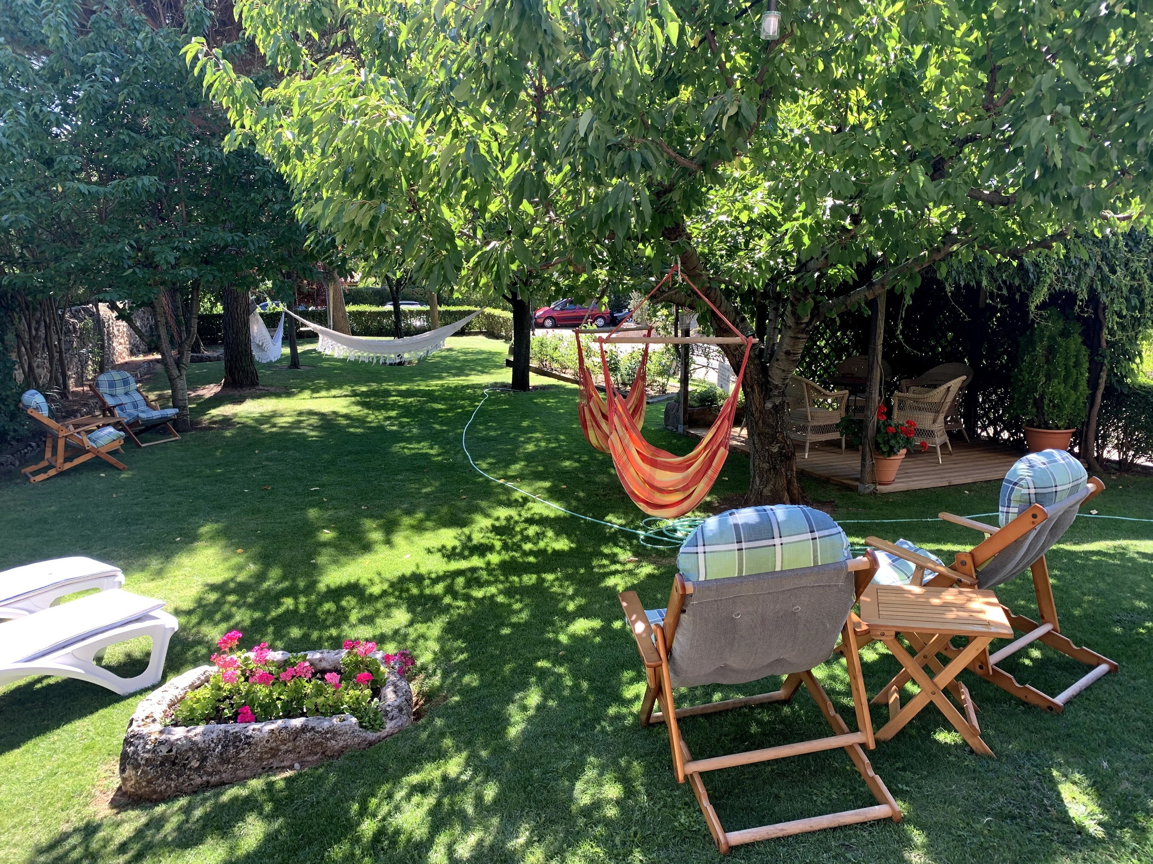 Un jardín cuidado con mobiliario exterior, incluyendo sillas y una hamaca, bajo un gran árbol.