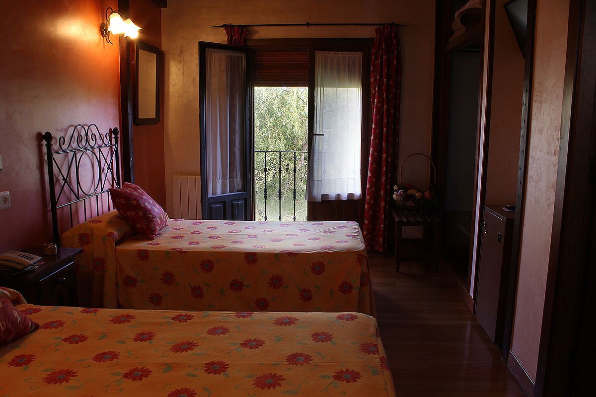 A room with two beds, a balcony, and a small table with a chair.