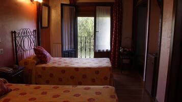 A room with two beds, a balcony, and a small table with a chair.