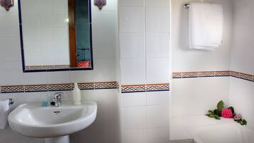 Un baño con lavamanos blanco, espejo y paredes con azulejos.