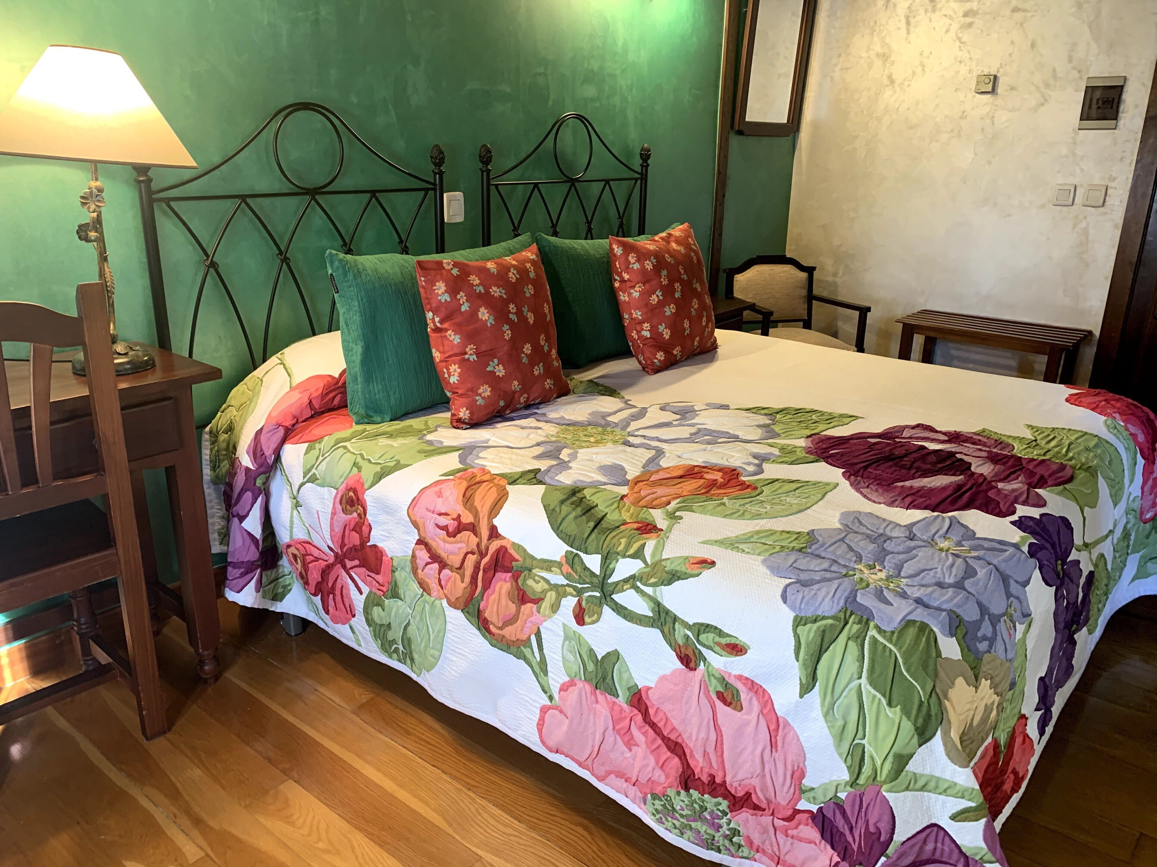 Ein Schlafzimmer mit einem blumigen Bettüberwurf, einem Holznachttisch, einer Lampe und einer grünen Wand.