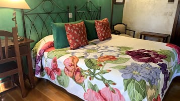 Ein Schlafzimmer mit einem blumigen Bettüberwurf, einem Holznachttisch, einer Lampe und einer grünen Wand.