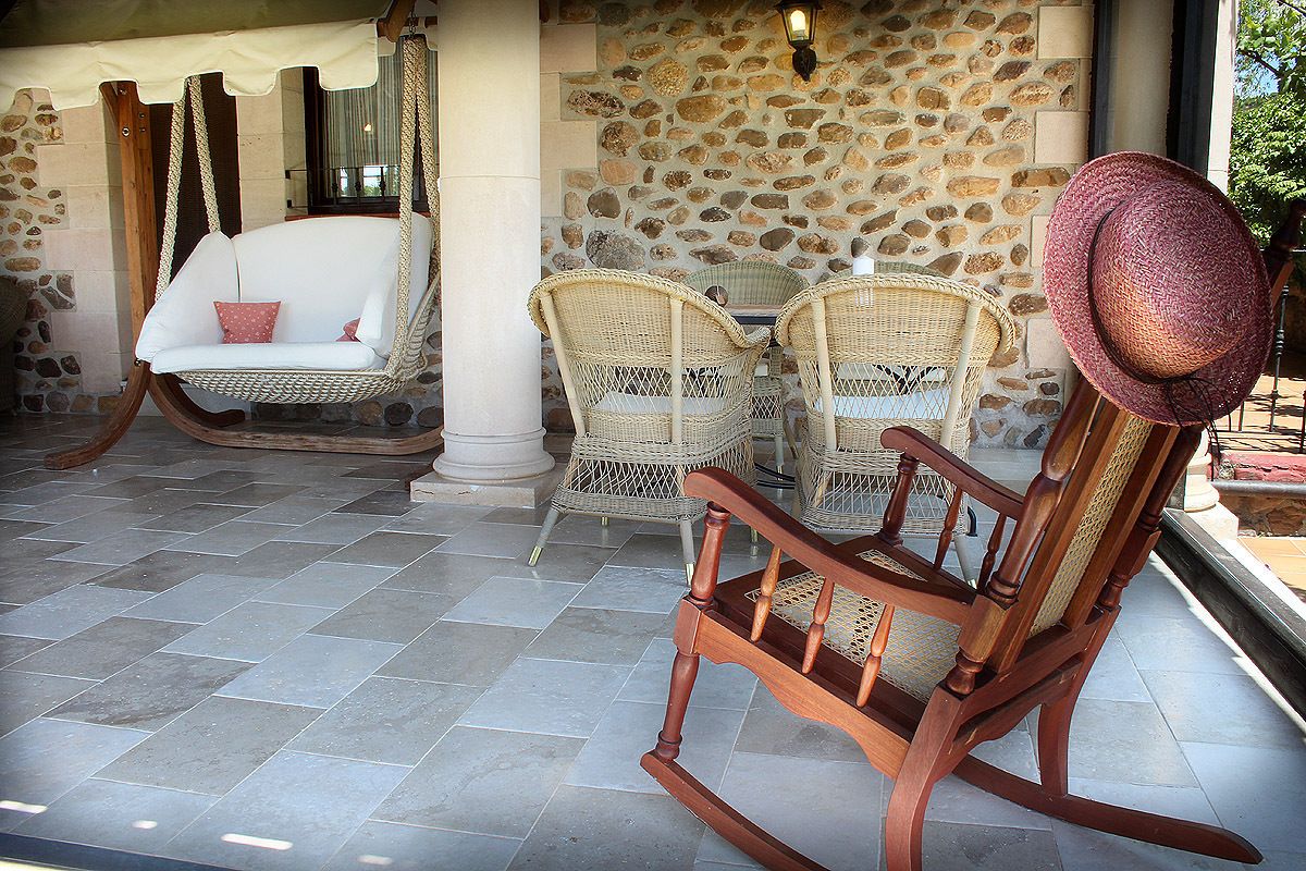 Un patio con mobiliario de mimbre, una mecedora y un muro de piedra.