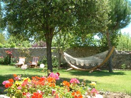 A hammock under a tree, a stone wall, and a grassy area with flowers.