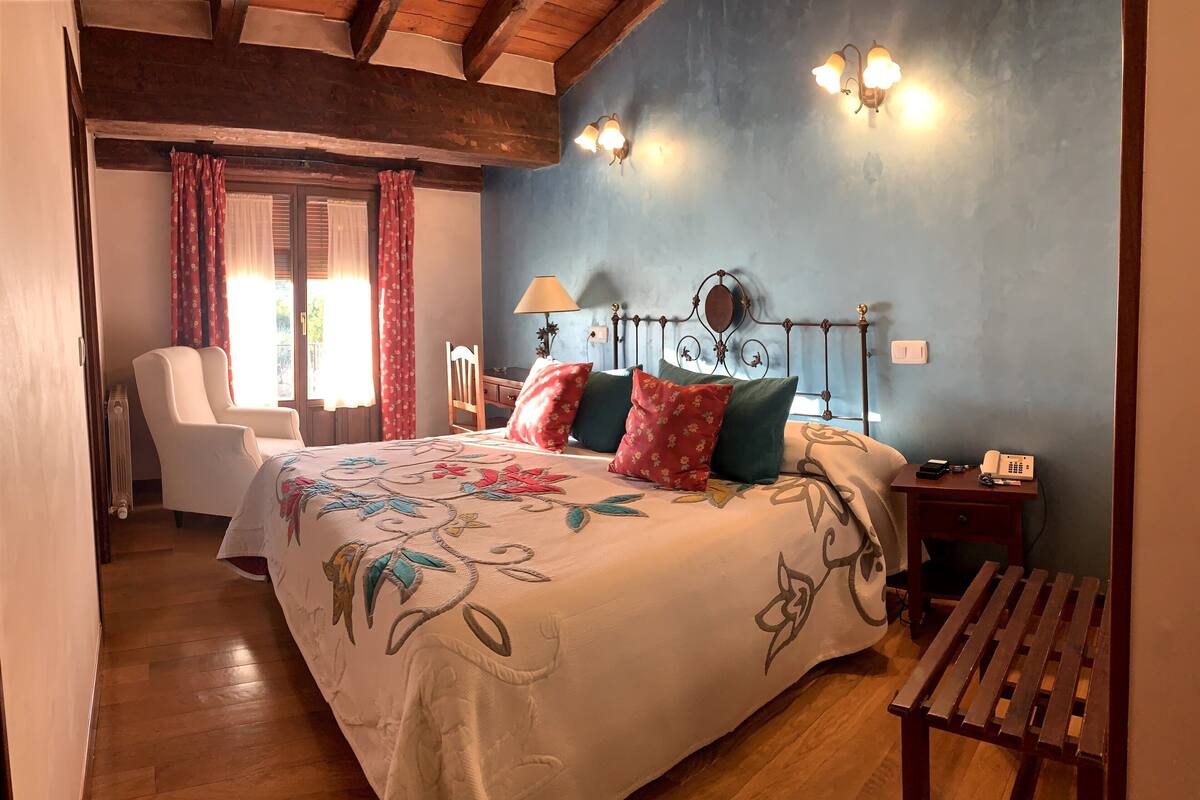 A bedroom with a bed, a chair, a bedside table with a lamp, and a wooden bench.