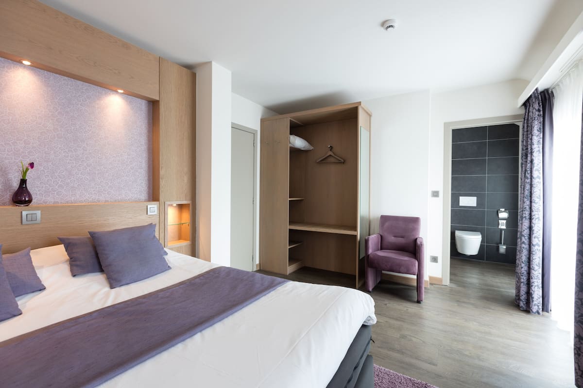 A modern hotel room with a large bed, a wardrobe, a seating area, and a bathroom.