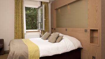 A bedroom with a large bed, a window with curtains, and a wooden headboard.