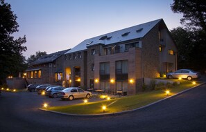 Un hotel de varios pisos con fachada de piedra, varios balcones y un estacionamiento con automóviles.