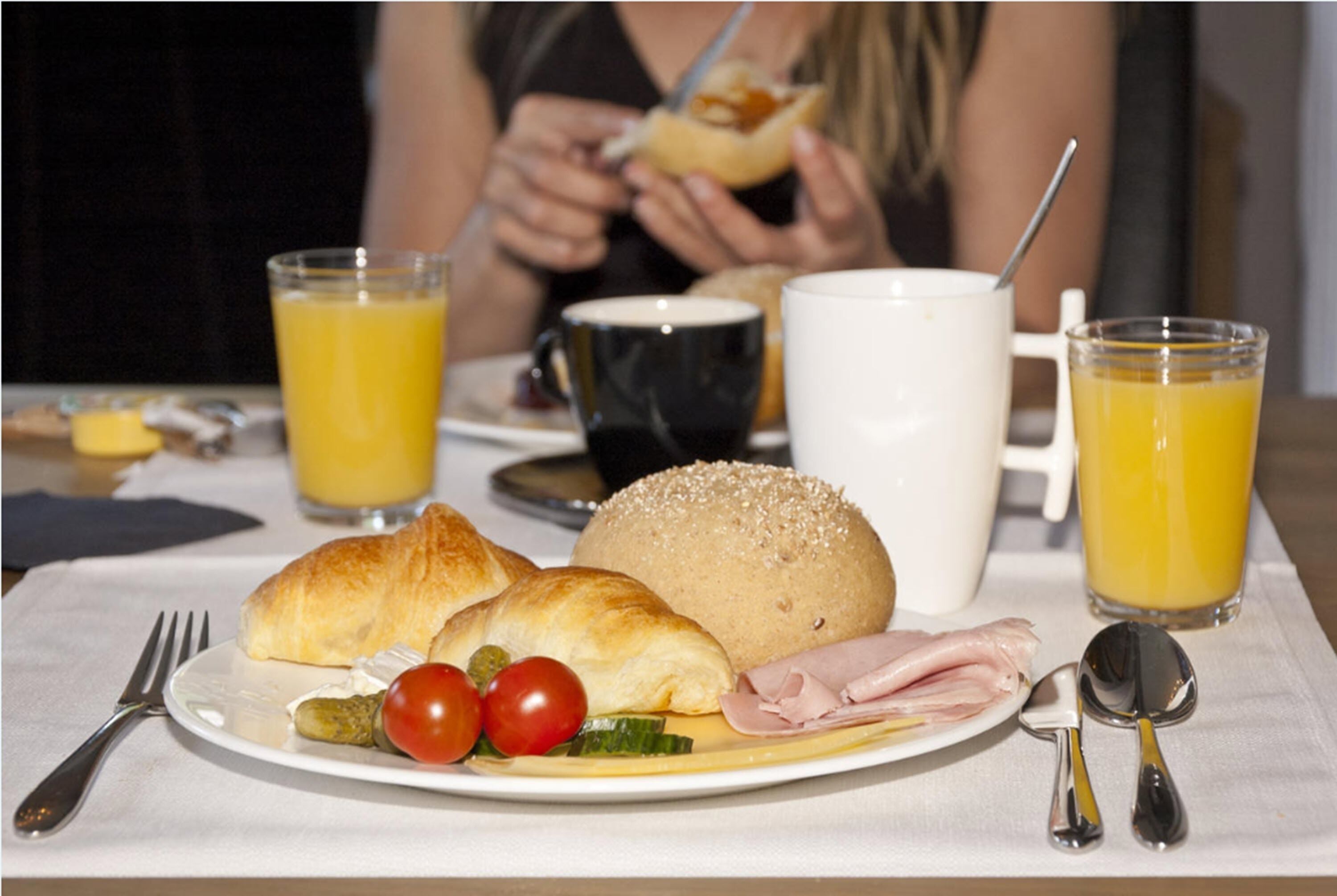 Een ontbijtbord met croissants, tomaten, kaas en ham, vergezeld van twee glazen sinaasappelsap en een witte mok.