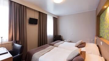 Een hotelkamer met twee bedden, een bureau, een stoel, een televisie en een raam met gordijnen.