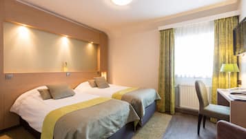 Habitación de hotel con dos camas, un escritorio, una silla y un ventanal con cortinas.