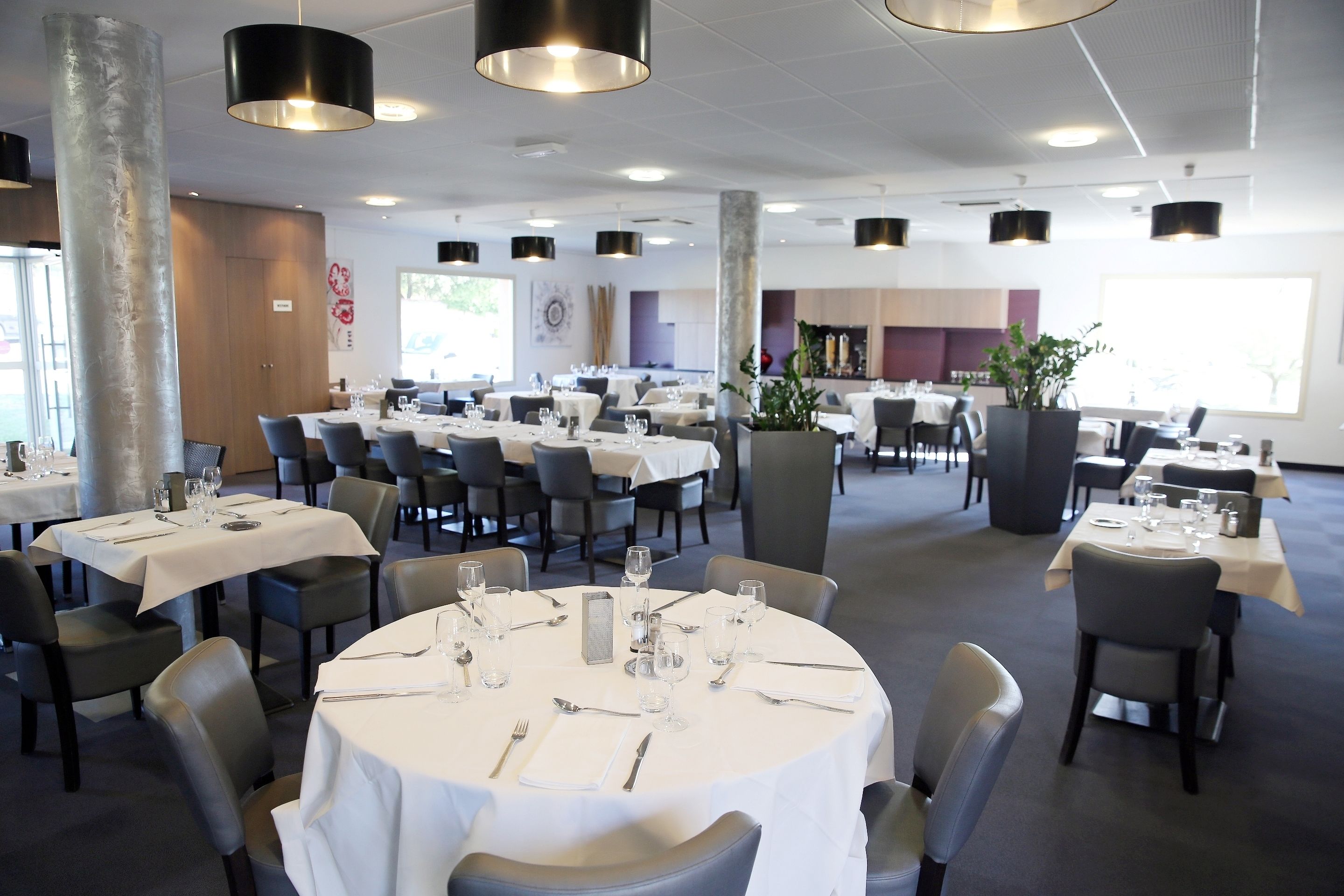 A restaurant with round tables set for dining, featuring a modern interior with pendant lighting and a neutral color palette.