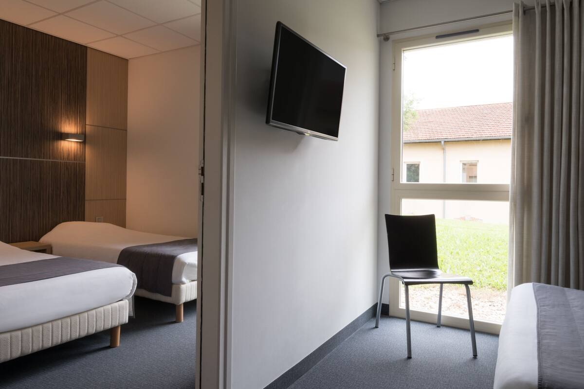 Habitación de hotel con dos camas, televisión, una silla y ventana con vistas.