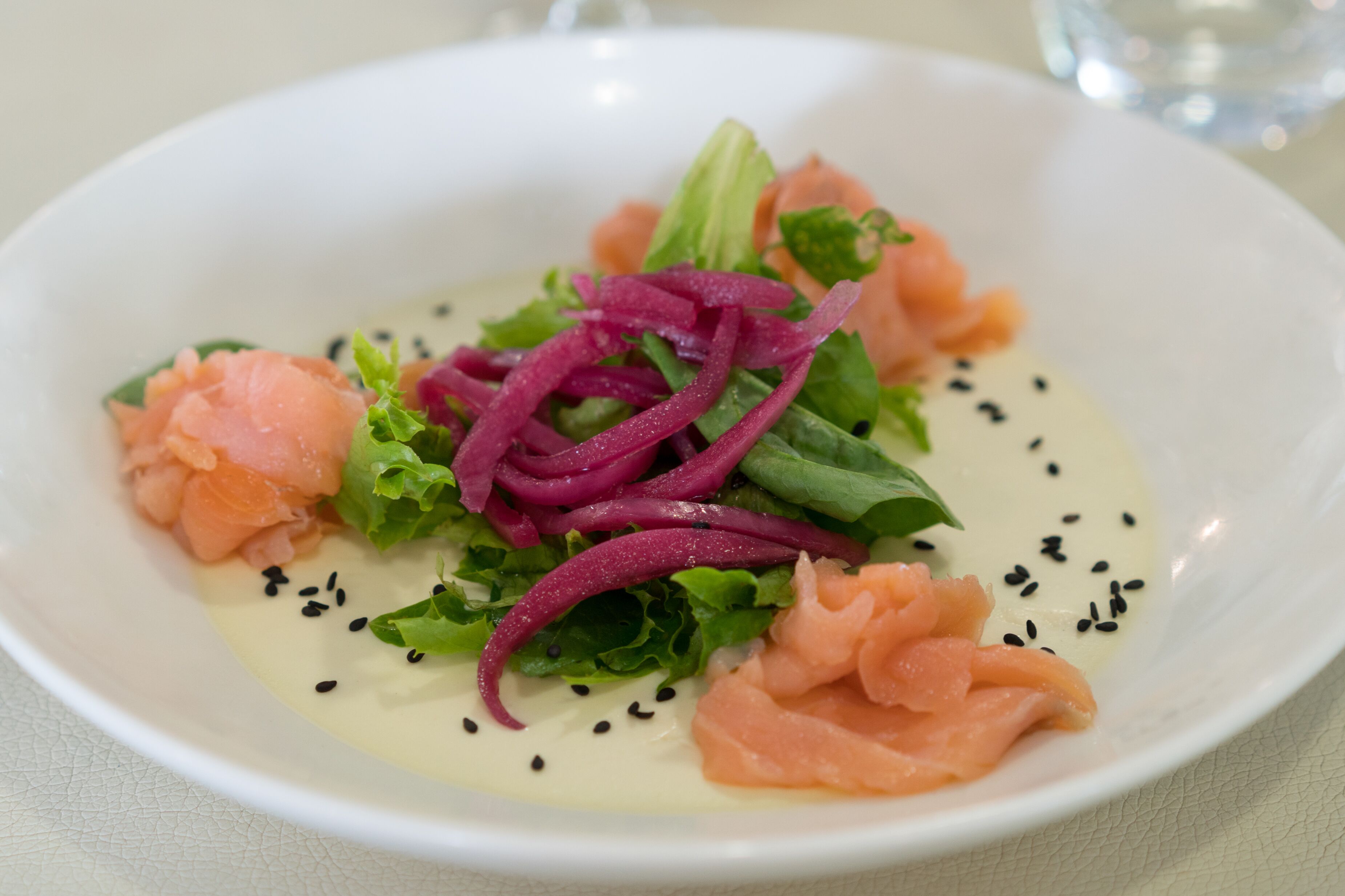 Un tazón blanco con una ensalada de salmón, lechuga y cebolla roja, decorada con semillas de sésamo negro.