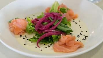 A white bowl with a salad containing salmon, lettuce, and red onion, garnished with black sesame seeds.