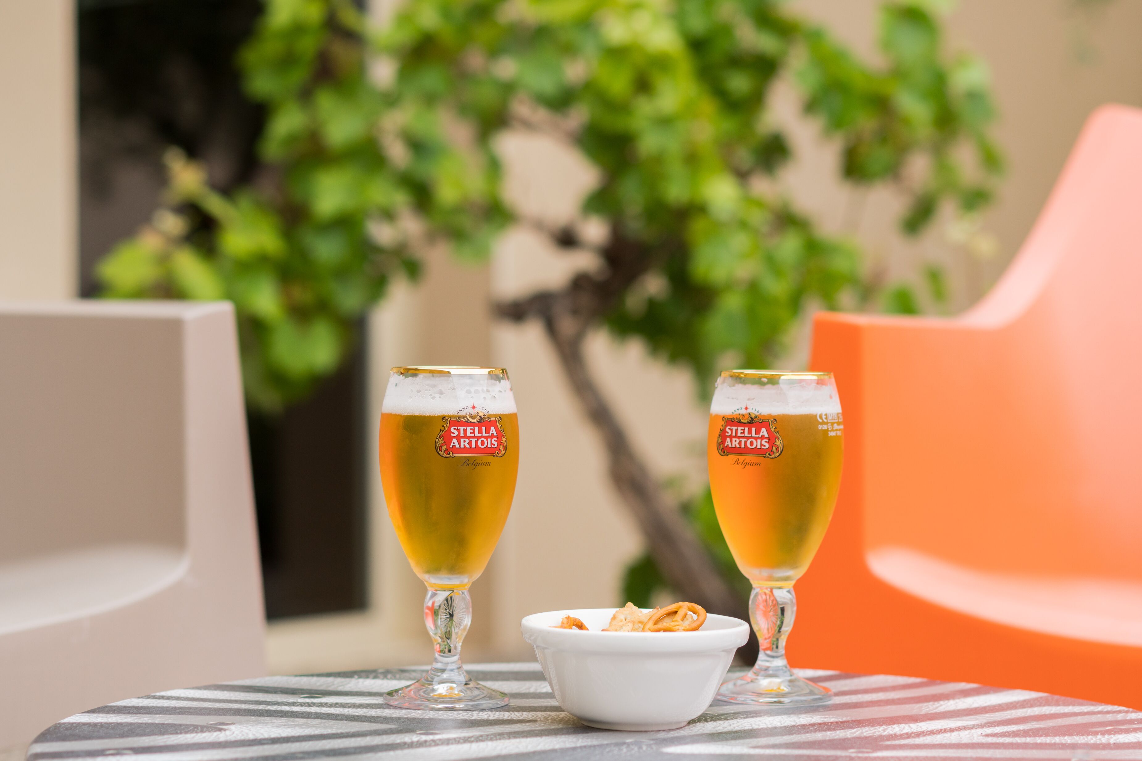 Dos vasos de cerveza sobre una mesa con un bol de aperitivos.