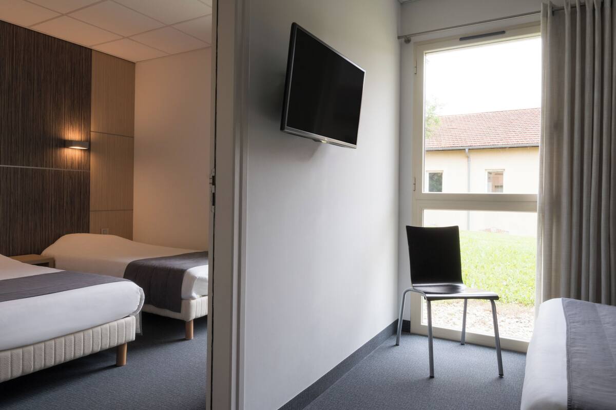 Habitación de hotel con dos camas, televisión, una silla y ventana con vistas.