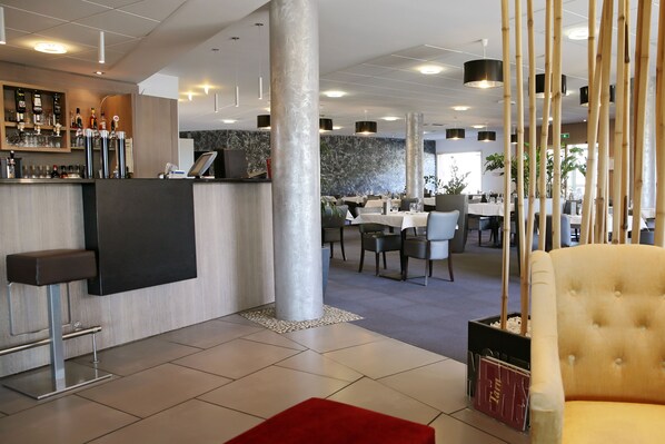 A modern hotel lobby with a reception desk, seating area, and dining space.