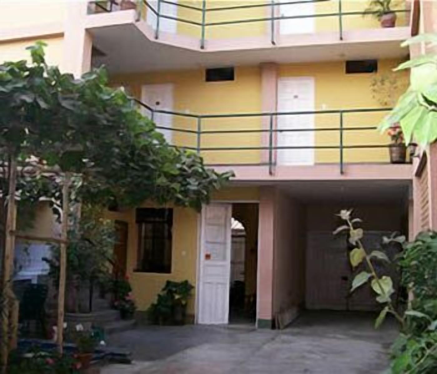 A multi-story building with balconies, a central door, and surrounding greenery.