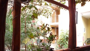 A view through a bamboo-framed window with a balcony, potted plants, and a building with a yellow facade in the background. - Hostal Tambo Colorado (Pisco)