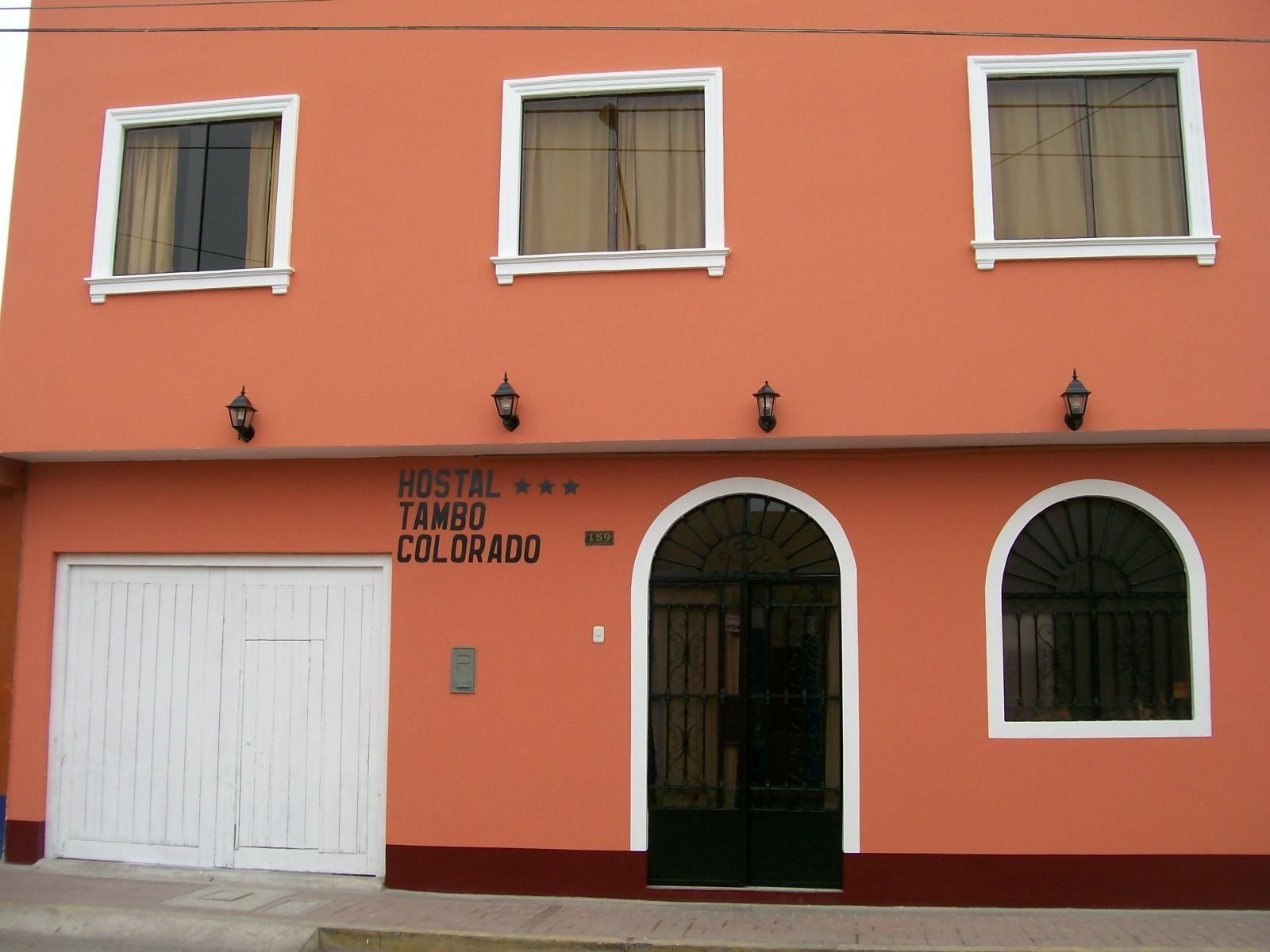 A building with a sign reading "HOSTAL TAMBO COLORADO" and three windows with white frames.