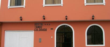 A building with a sign reading "HOSTAL TAMBO COLORADO" and three windows with white frames.