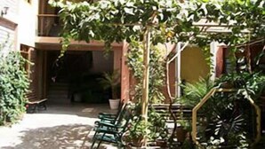 A multi-story building with balconies and a covered outdoor seating area with chairs and potted plants. - Hostal Tambo Colorado (Pisco)