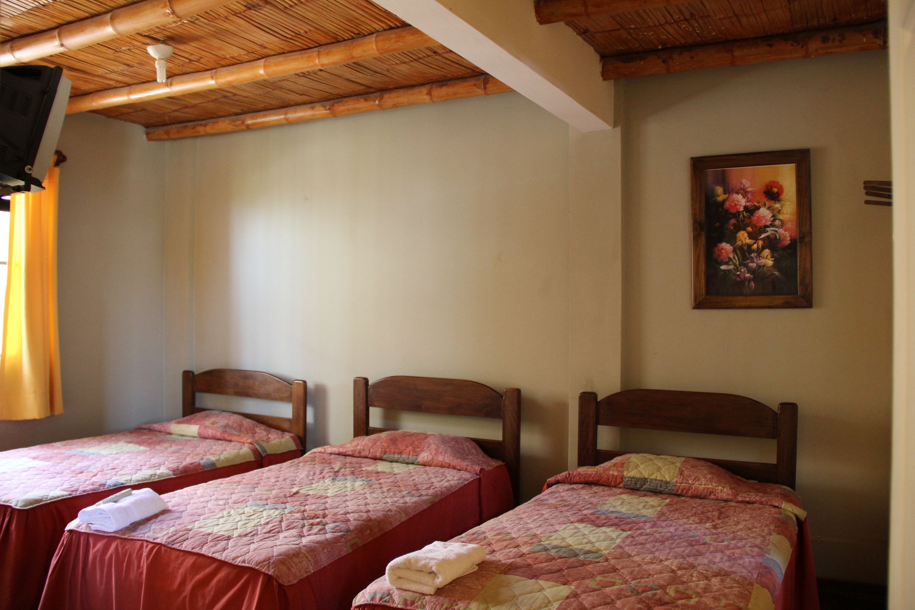A room with two single beds, wooden headboards, a bamboo ceiling, and a floral painting on the wall.